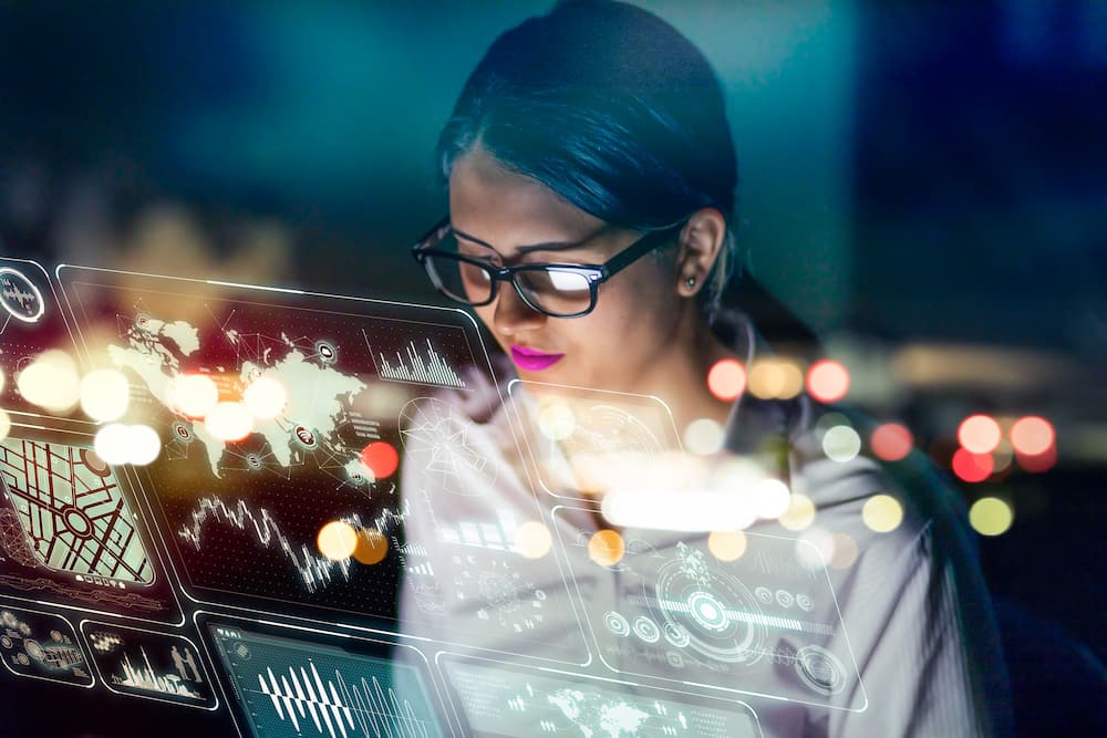 a woman working at a futuristic computer while large screens display vital information